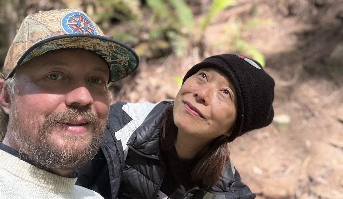 Two friends among redwoods, one looking up into the canopy.