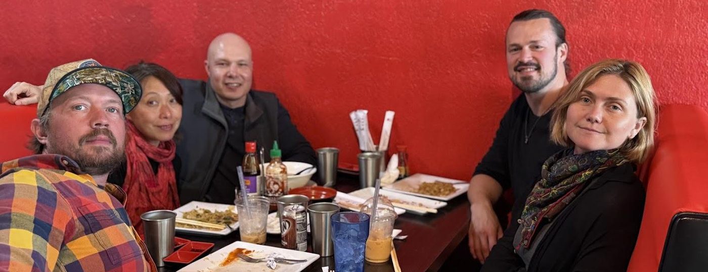 Five friends around a restaurant table against a bright red wall.
