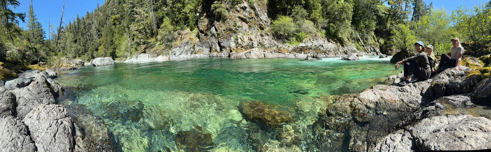 A quiet Crescent City river pool, turquoise water over rocks, framed by redwood forest.